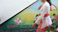 Seorang perempuan berjalan di depan mural pelarangan plastik. Kredit foto: NPAP